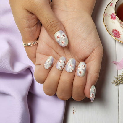 Close-up of a hand with floral nail design holding another hand, with a teacup in the background.