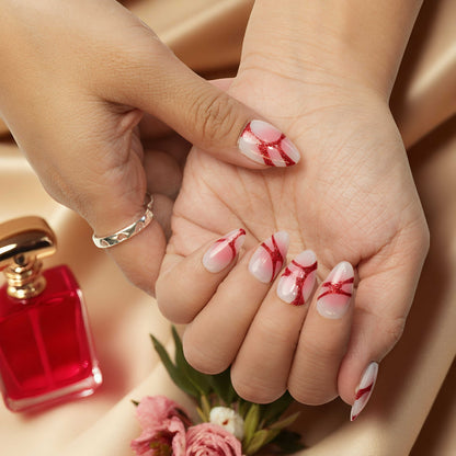 Handmade glue on nails in glossy red and pink tones, laid across floral satin with perfume props, showcasing fake nail detailing.