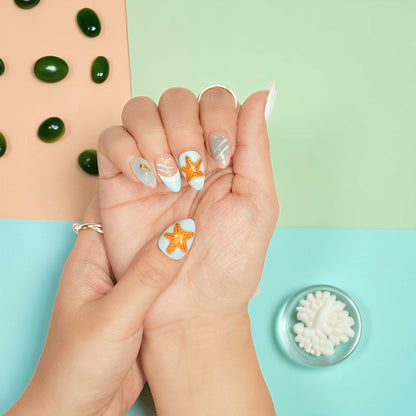 Short almond artificial nails featuring golden shell charms, soft swirl art, and pastel beach colours.
