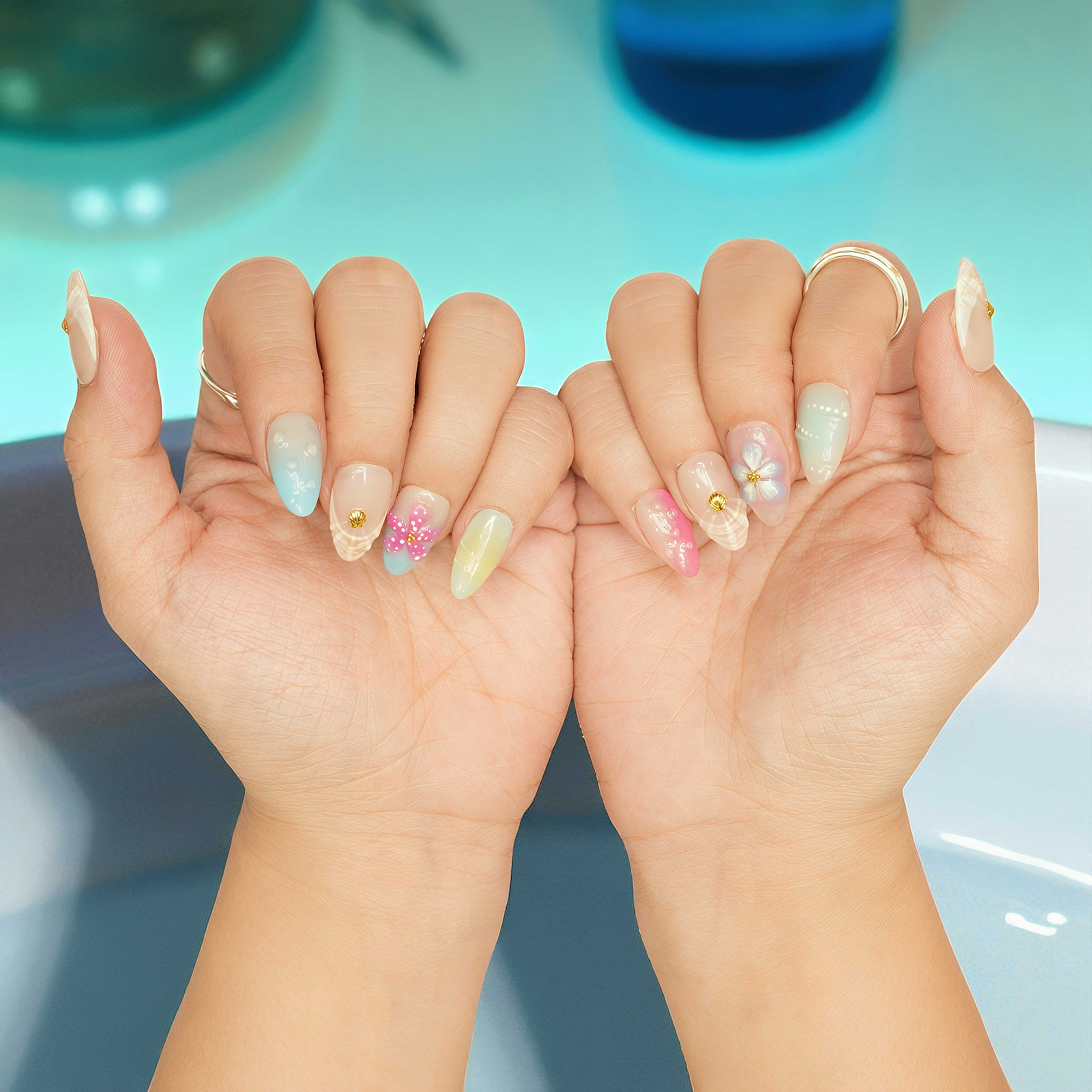 Close-up of short almond press on nail with pink 3D flower, gold shell charm, and pastel blue ombre,  inspired by nail salon Adelaide styles.