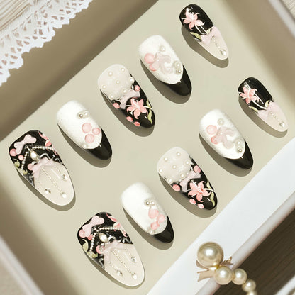 Artistic shot of black press on nails with pink lily flowers, chrome shimmer, and soft blush bow.