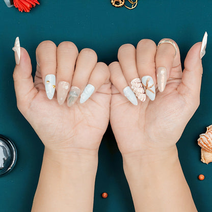 Jelly nails featuring golden seashell charm on nude and blue background