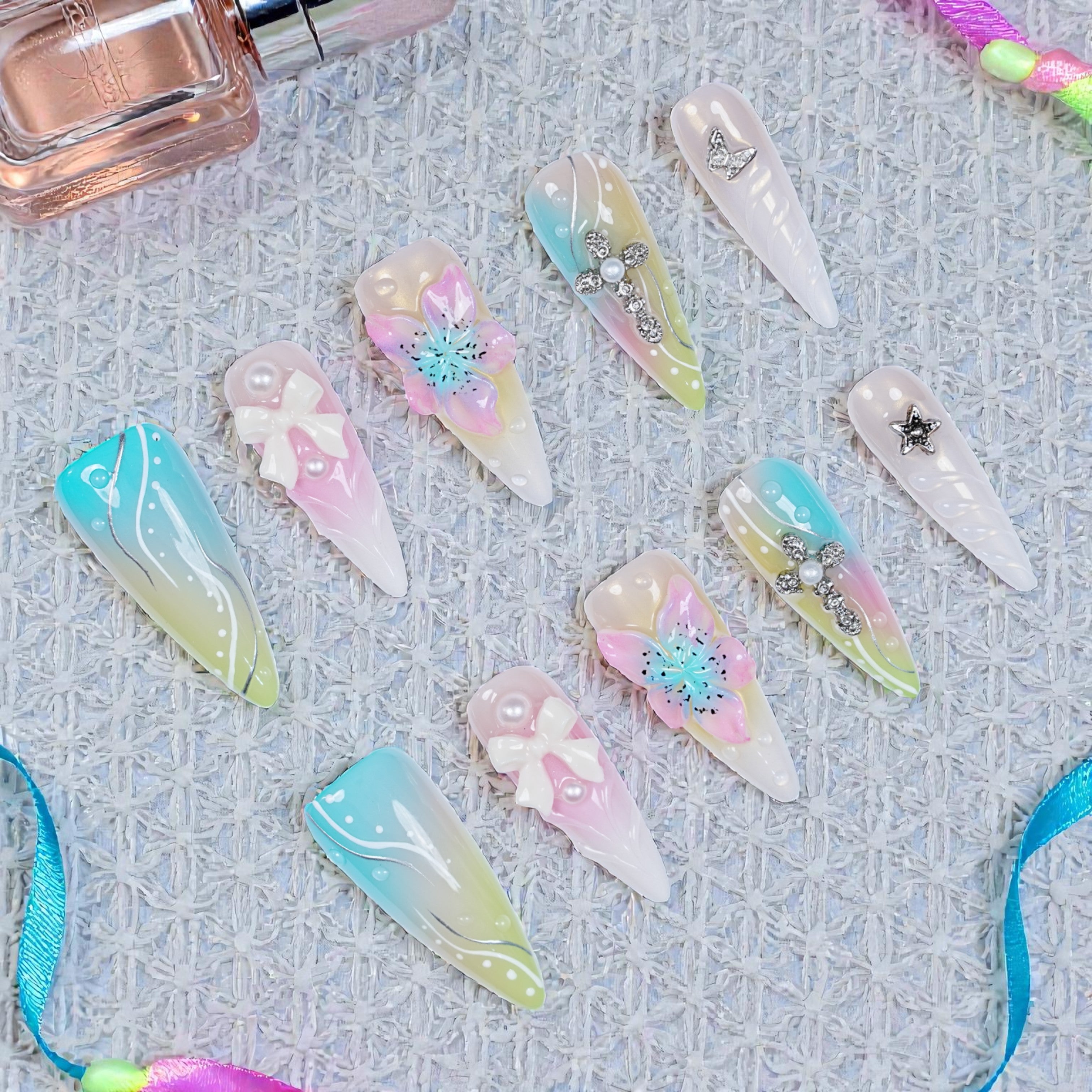 Aurora Belle Garden nail set with pastel jelly base, white floral embellishments, pearls, and gold cross details on long almond tips