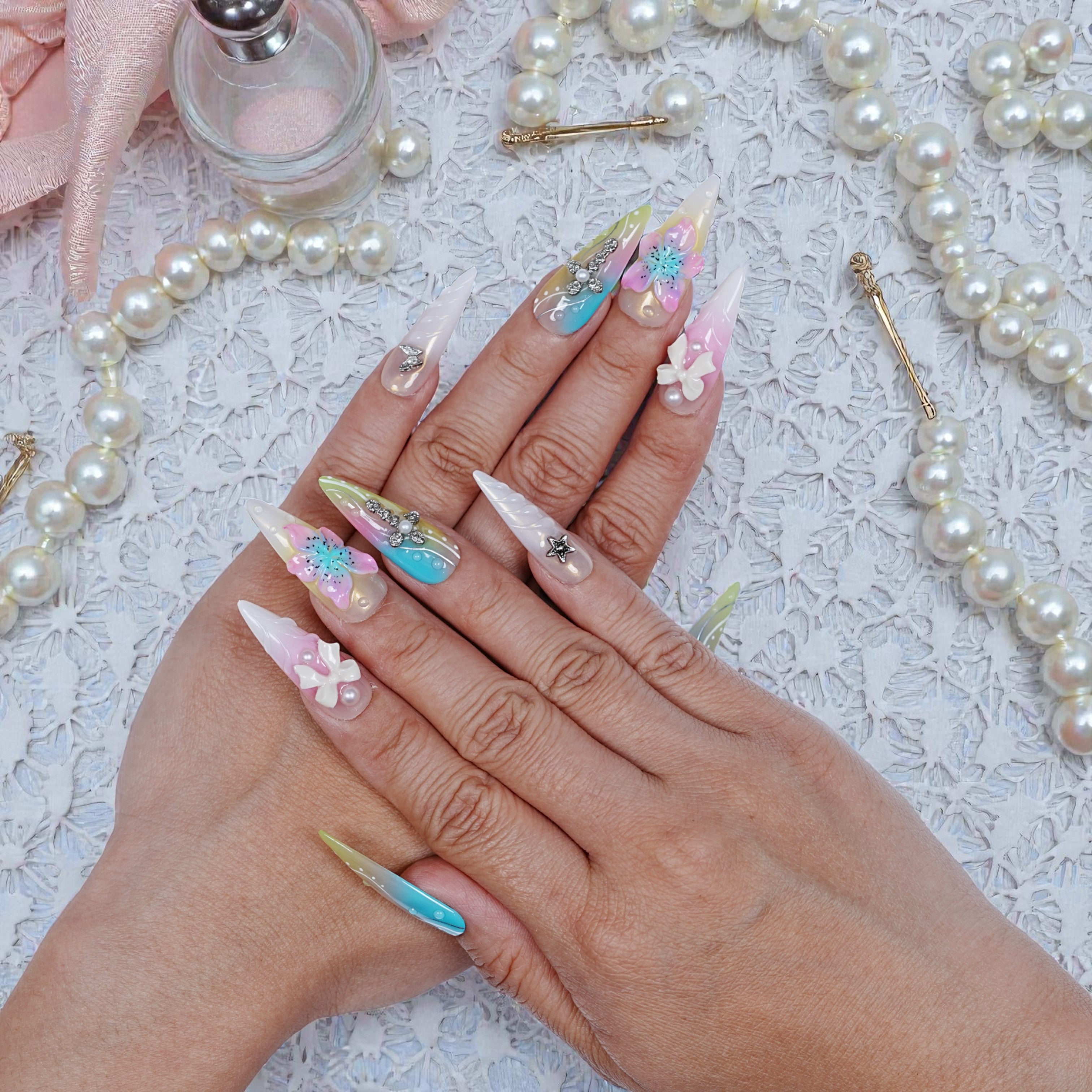 Both hands wearing Aurora Belle Garden nails, featuring a soft garden-inspired palette and sculpted embellishments