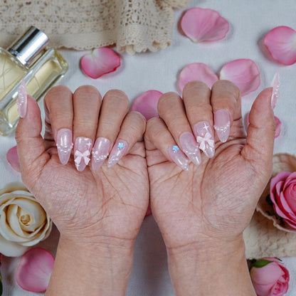 Close up of blush pink artificial nail set with pearl and bow designs on model hands