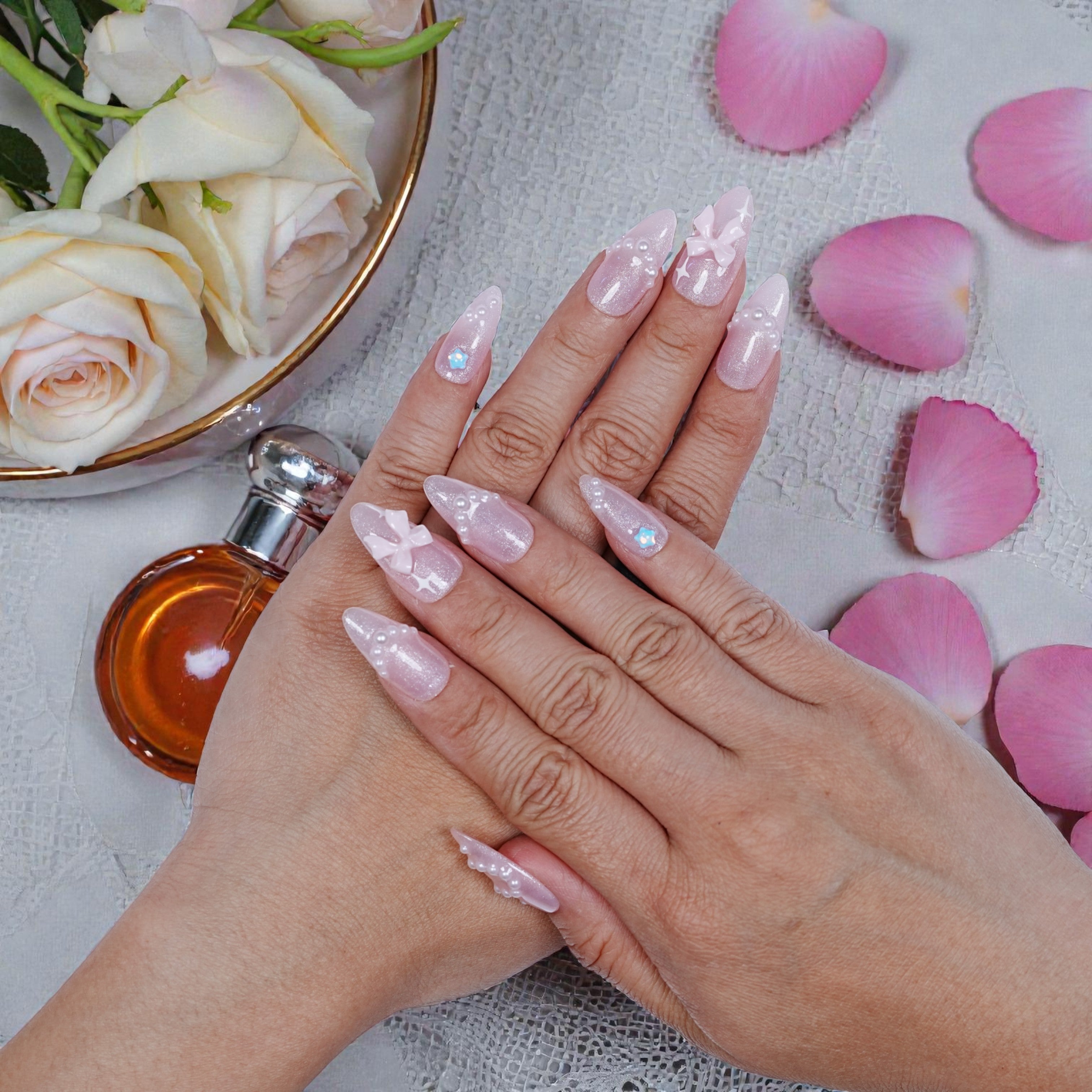 Hand model wearing blush artificial nails with petals and fragrance props