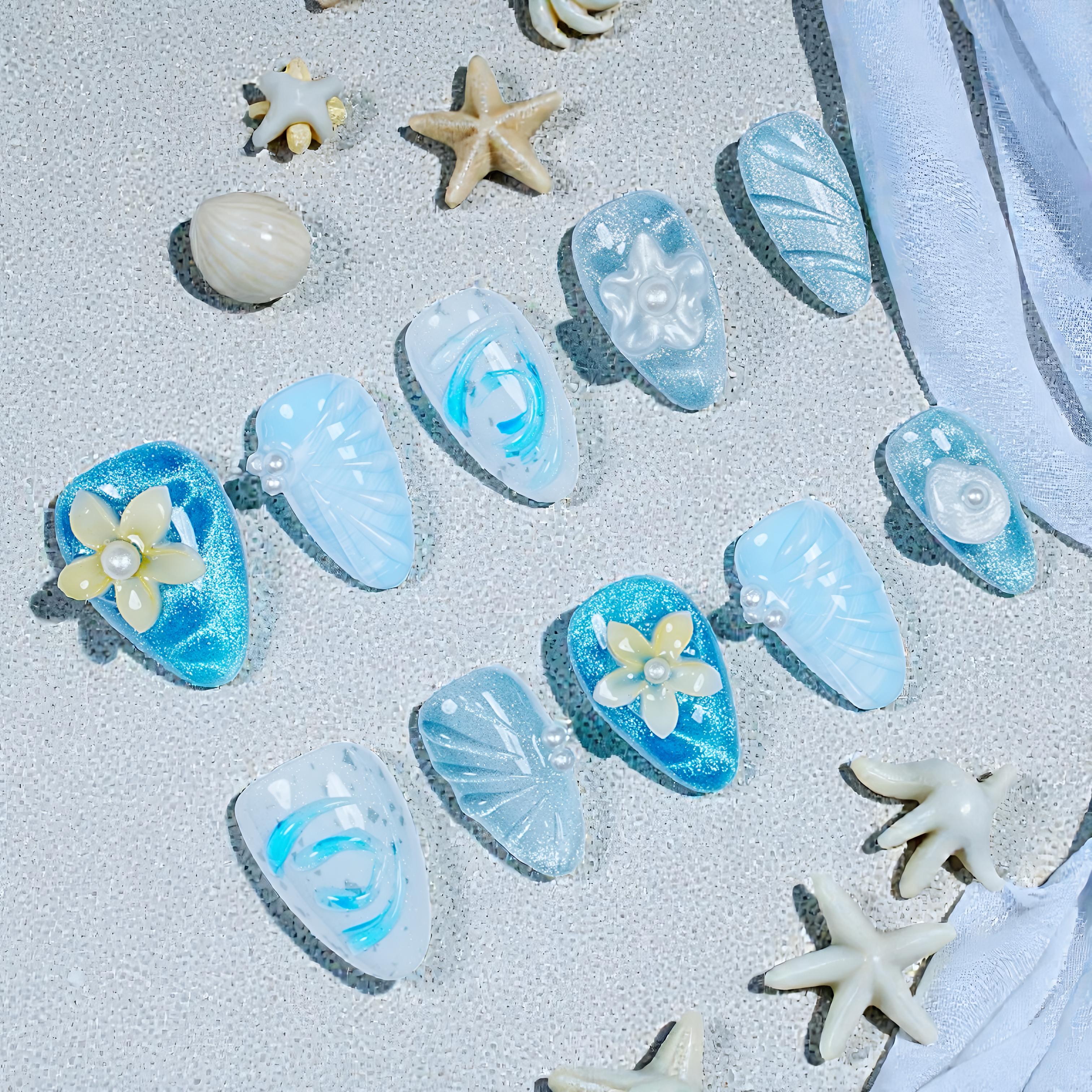 Handmade reusable press on nails in blue and white with pearl and flower designs, displayed with starfish and seashells