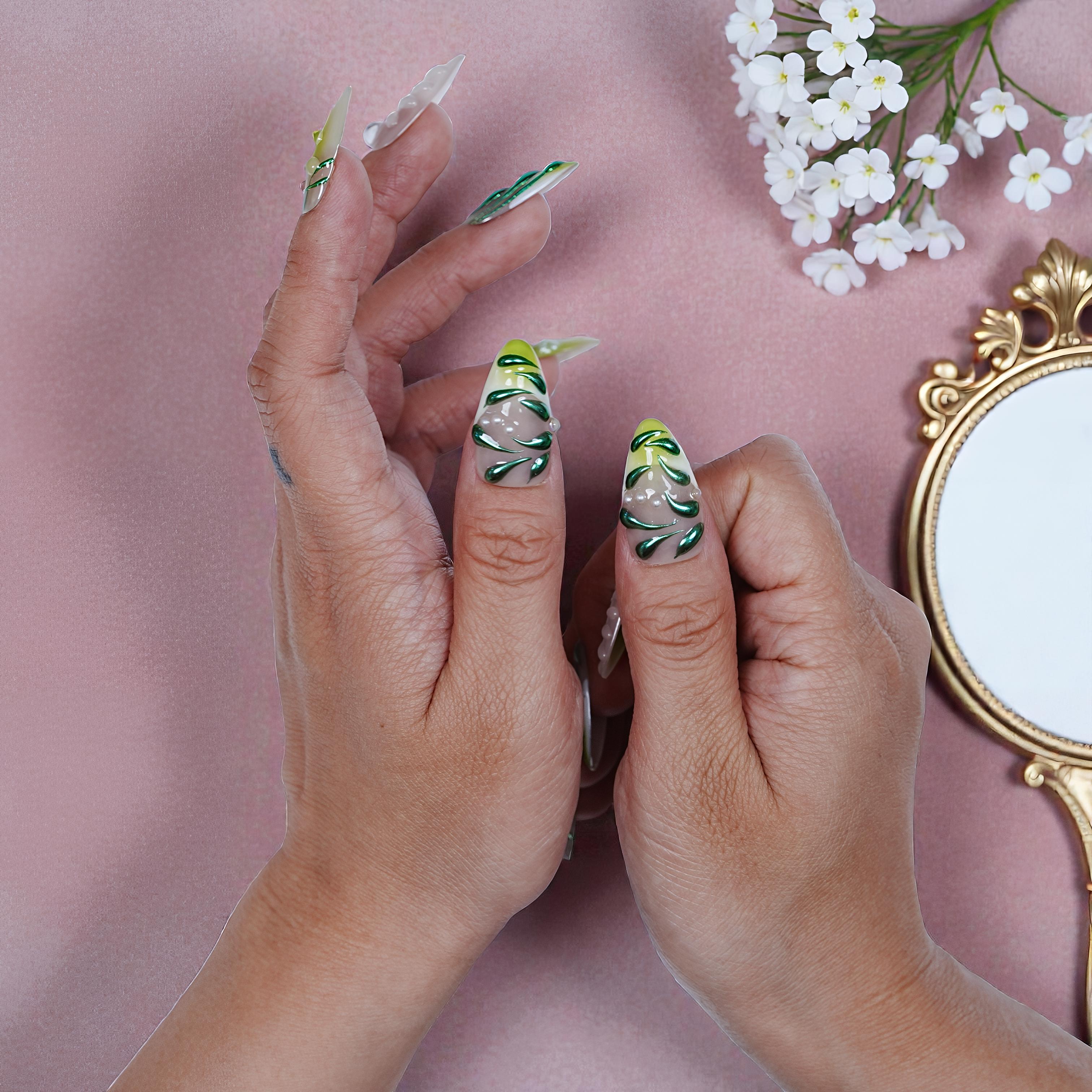 Hands with premium reusable press on nails featuring green leaf designs and pearl accents on pink background