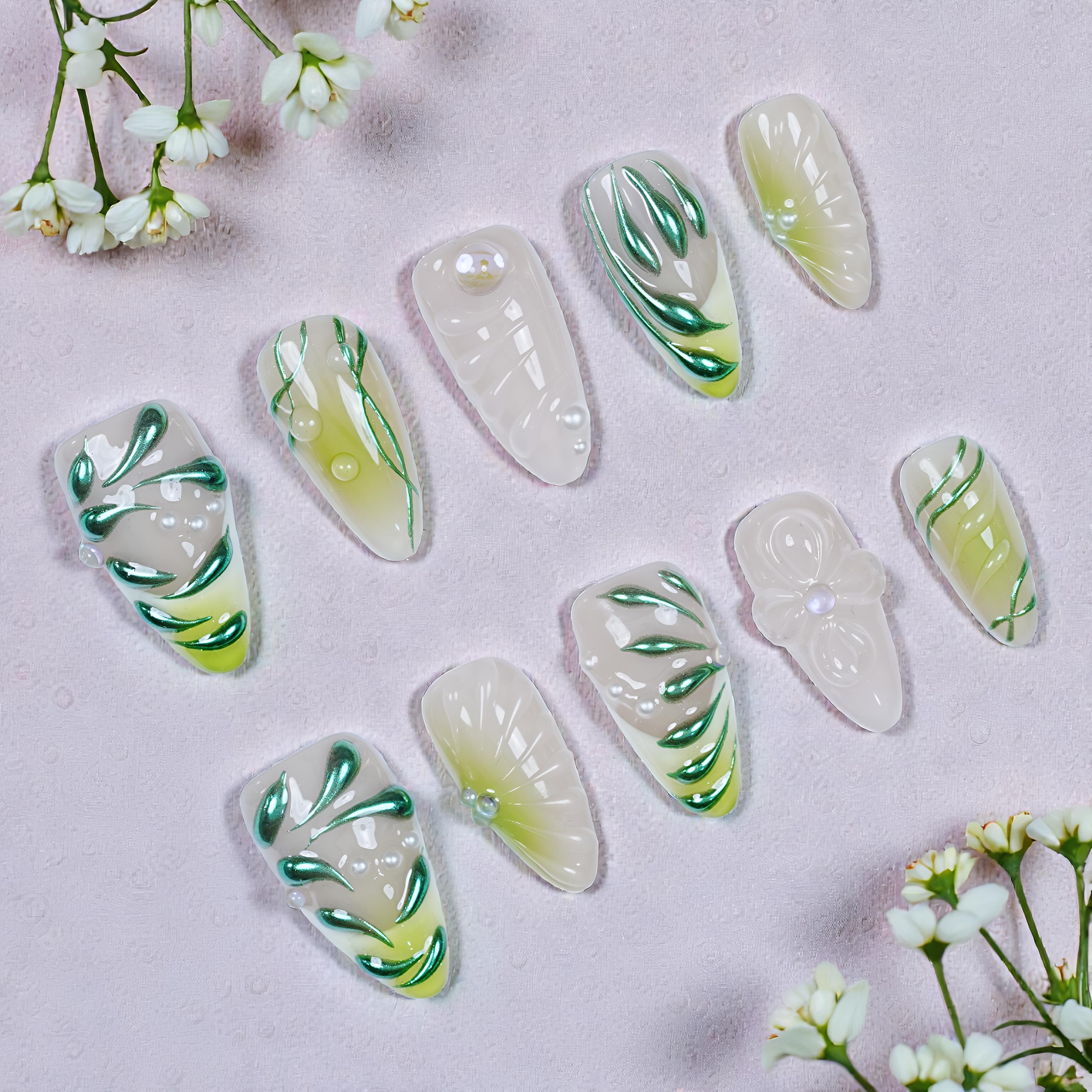 Set of reusable handmade press on nails with green botanical designs and pearl accents on light background