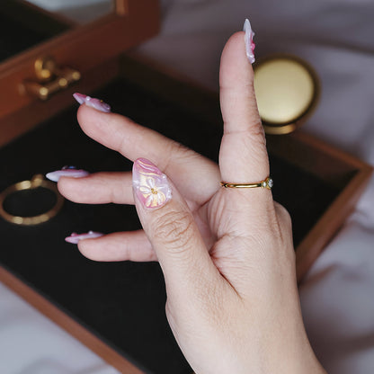 Side angle of hand showing swirl textures, 3D bows, and glossy shine in soft ombré pink.