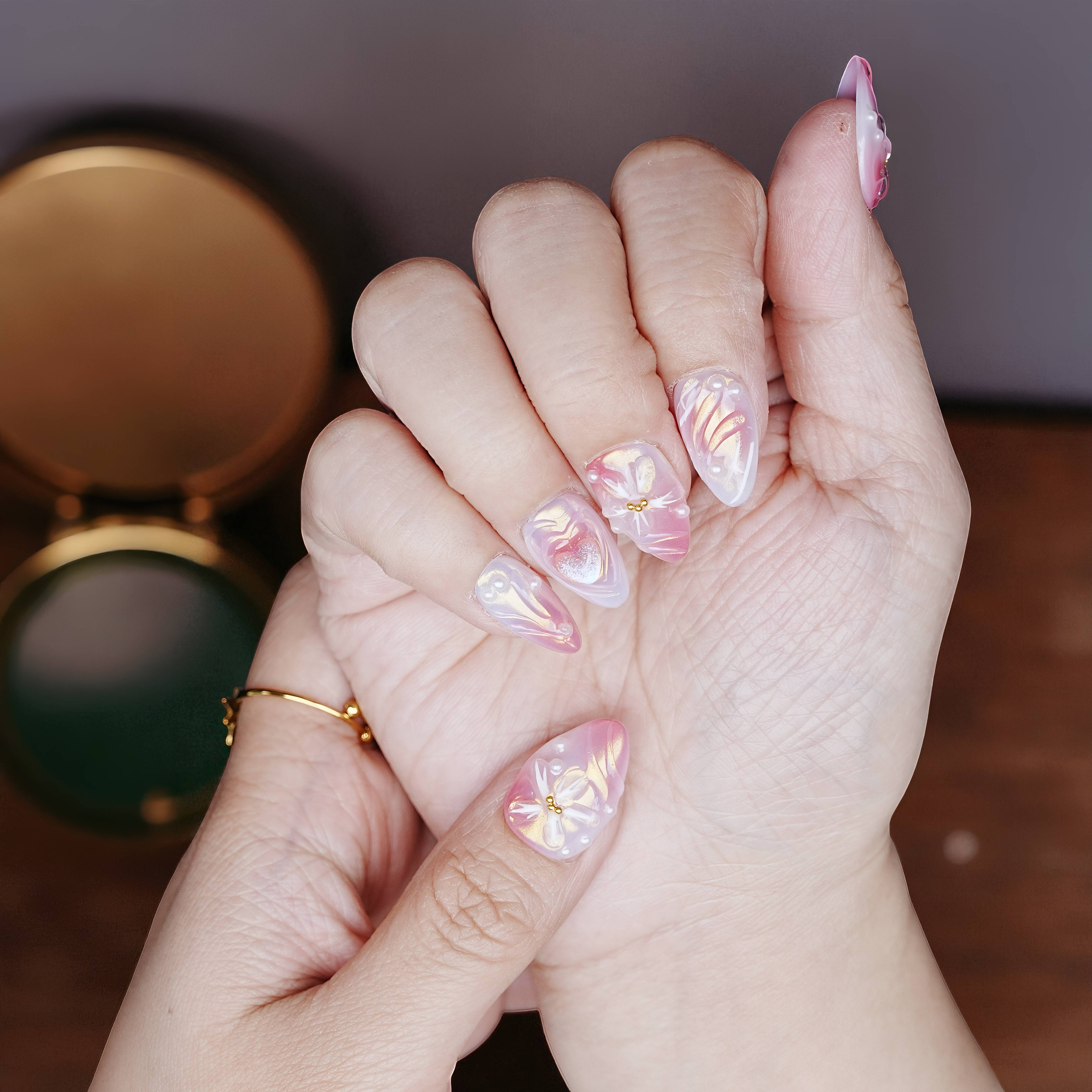 Close-up hand pose with sculpted shimmer nails, ombré pink to purple finish, and pearl embellishments.