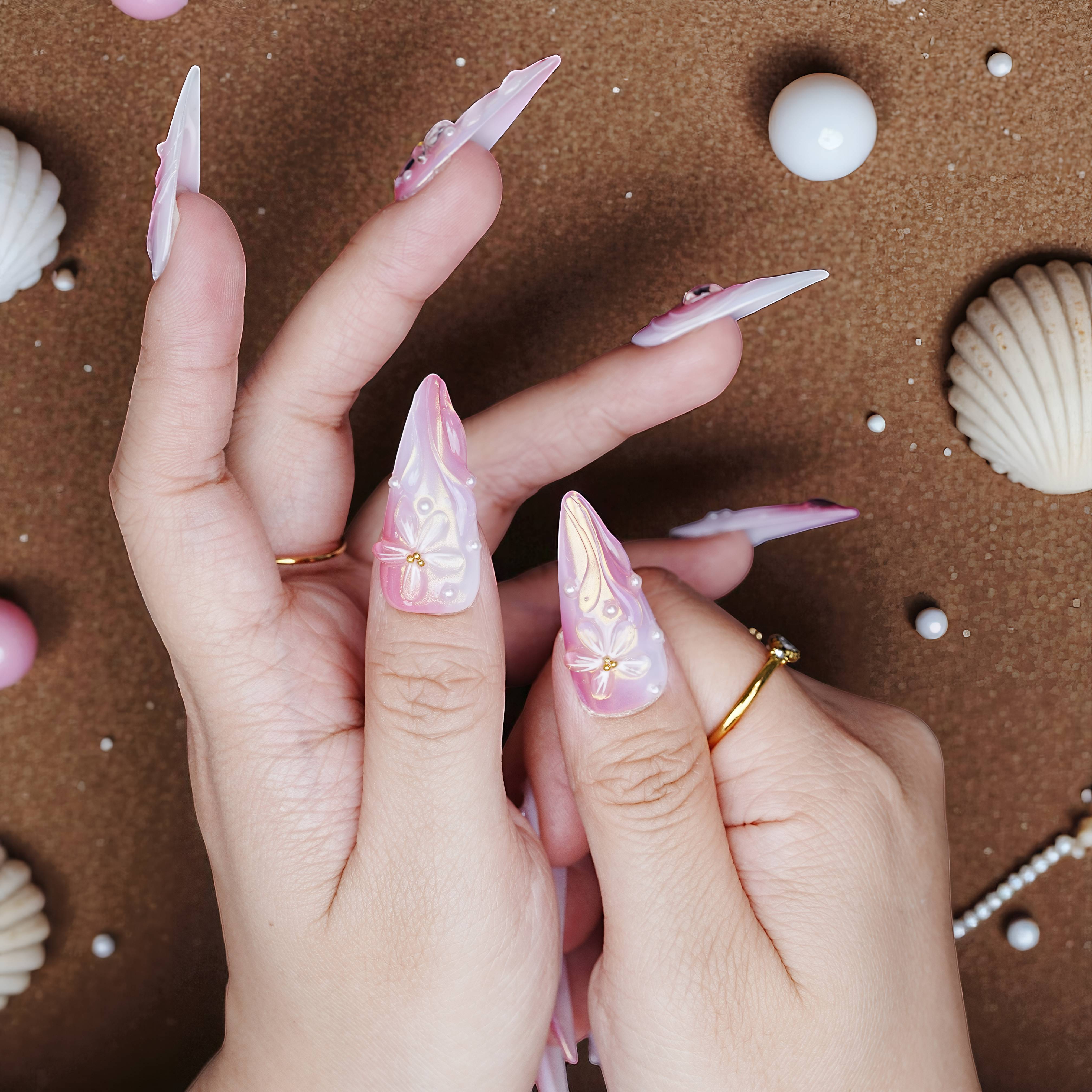 Close-up of thumbs featuring pink and white press on nails with sculpted flowers and pearl embellishments