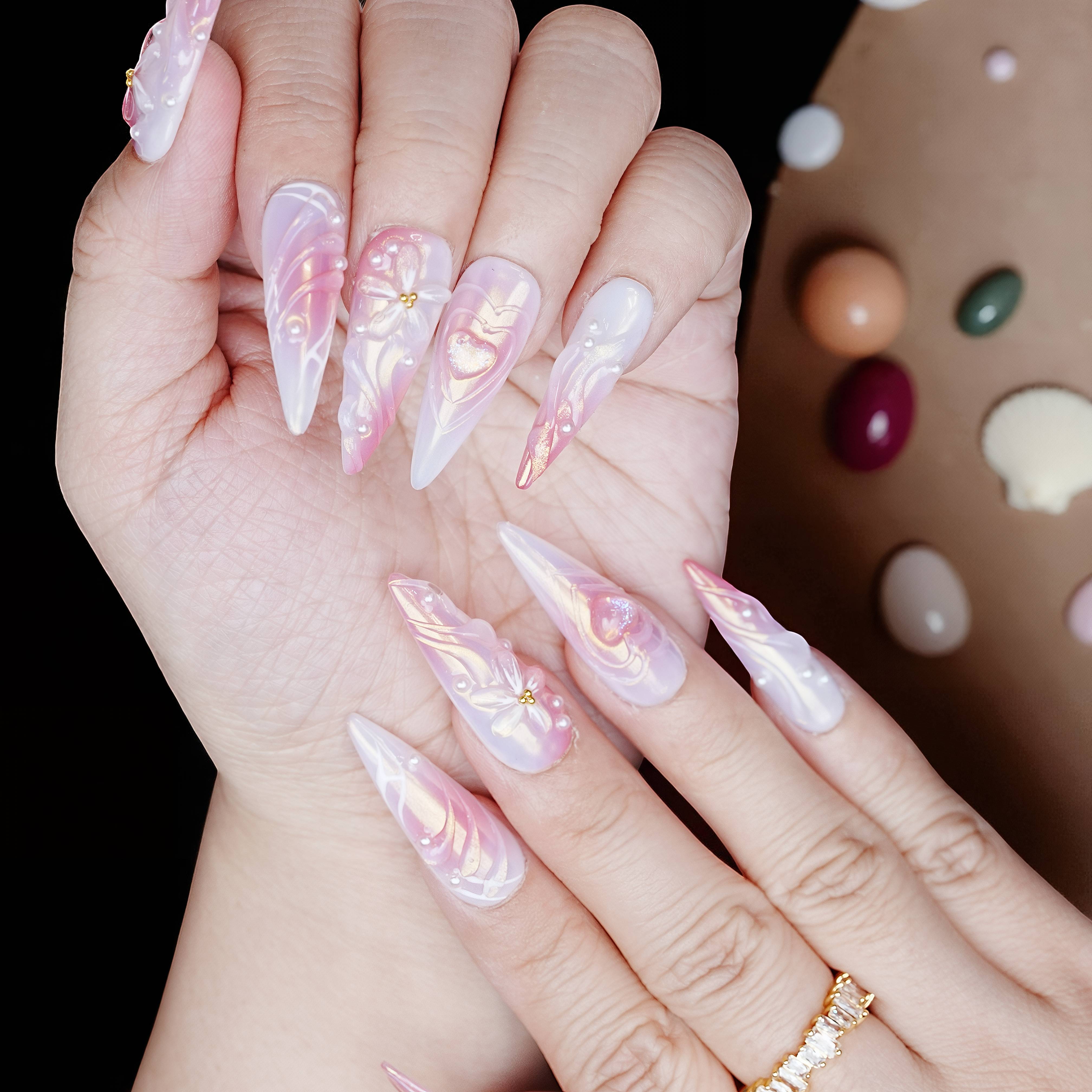 Side view of long glossy pink and white stiletto press on nails with 3D hearts and pearl detailing