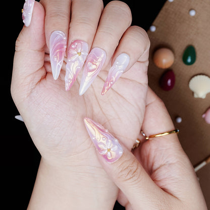 Angle view of pearlescent pink stiletto nails featuring sculpted bows, shimmer effects, and heart accents