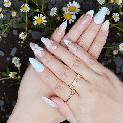 Hand pose showing full set of nude and baby blue press on nails with 3D daisy design and pearl textures.