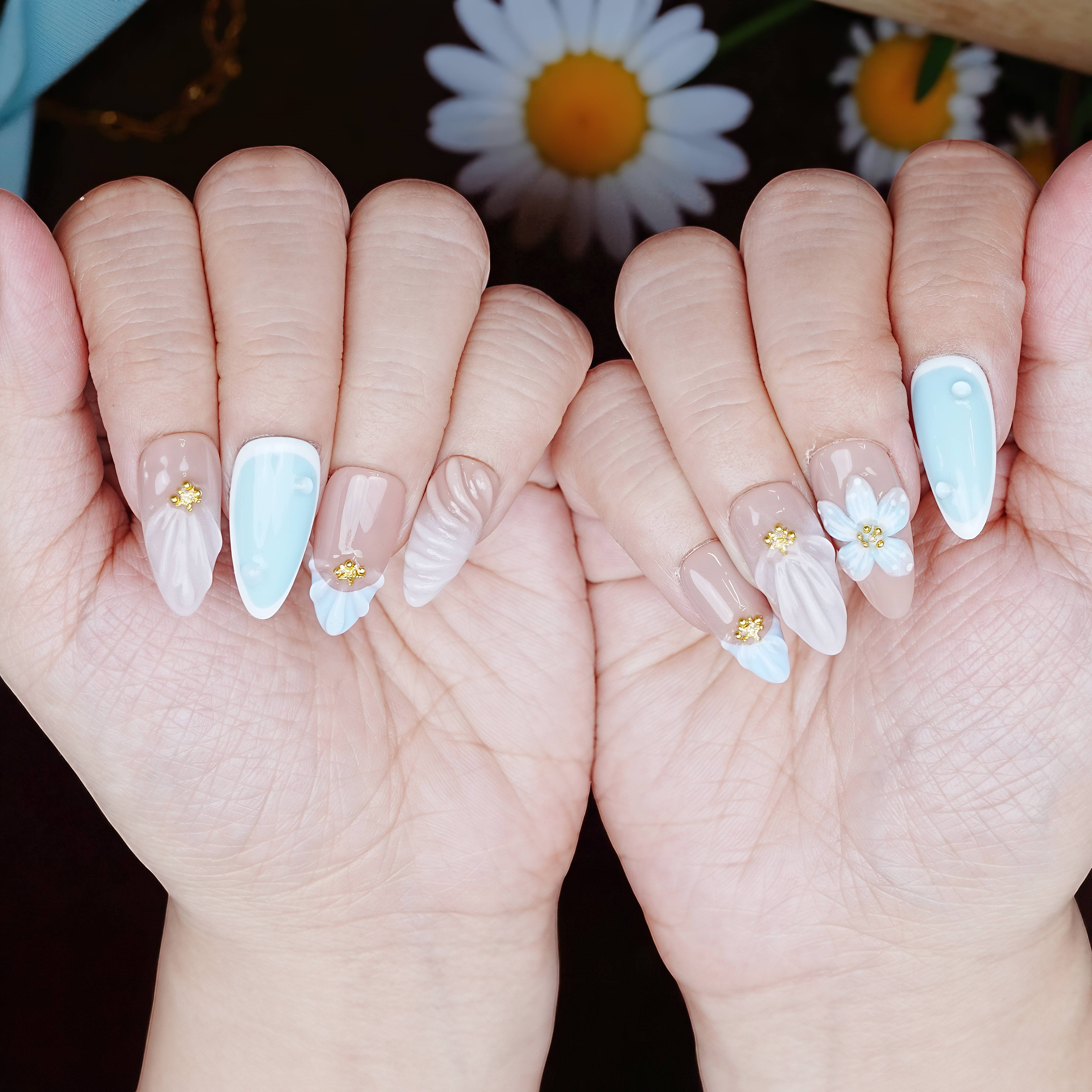 Both hands styled with complete Blue Daisy Shell set, posed over a daisy pattern with springtime detail.