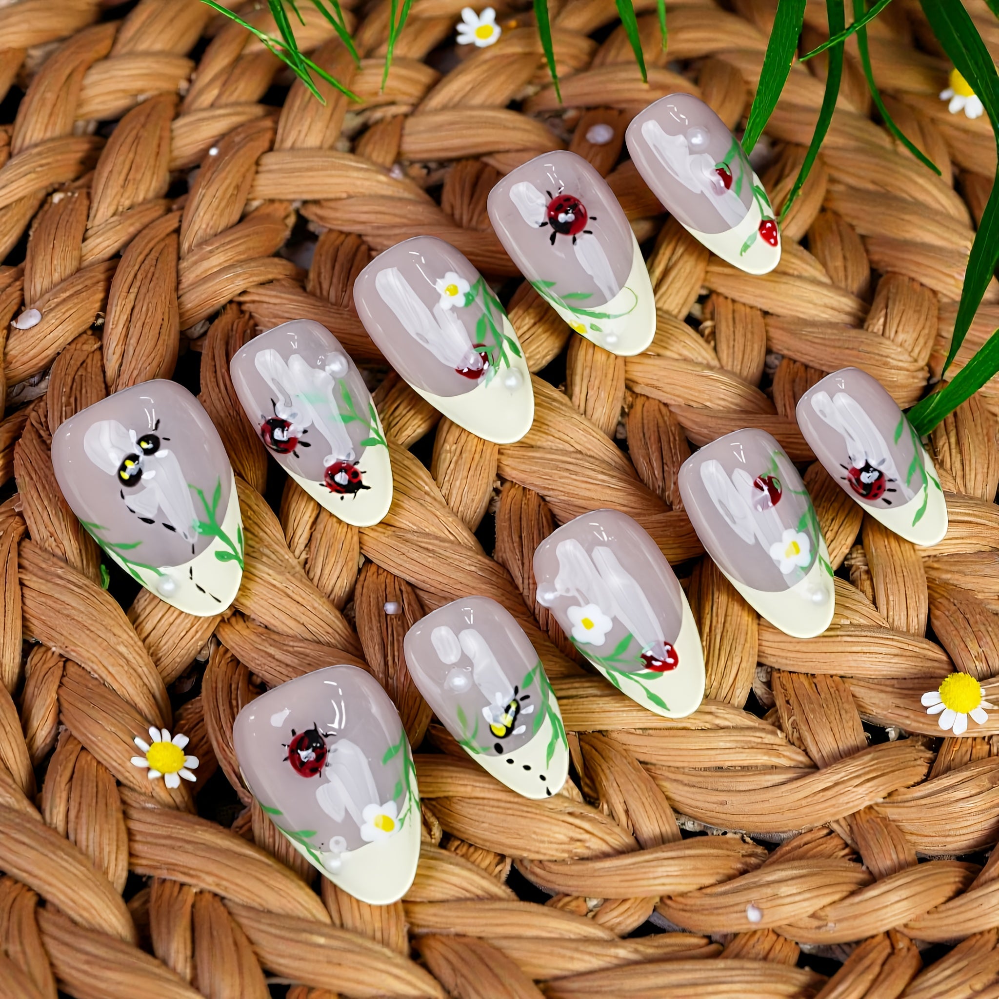 Top view of Garden Picnic press on nails featuring nude base, hand-painted ladybugs, bees, daisies, and green grass details on soft yellow tips.