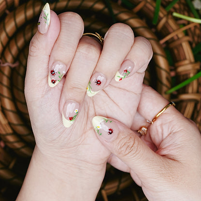 Close-up of ladybug press on nails with daisy accents and yellow tip details against woven background.