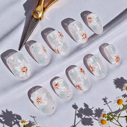 Handmade press on nails with white floral design and silver beads on glittery background, scissors nearby