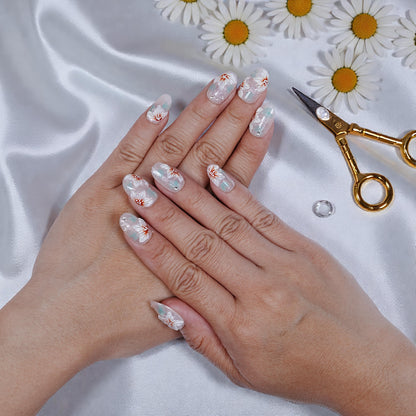 Hands with pastel blue and white floral press on nails featuring daisies, on satin background with scattered fresh daisies and gold manicure scissors