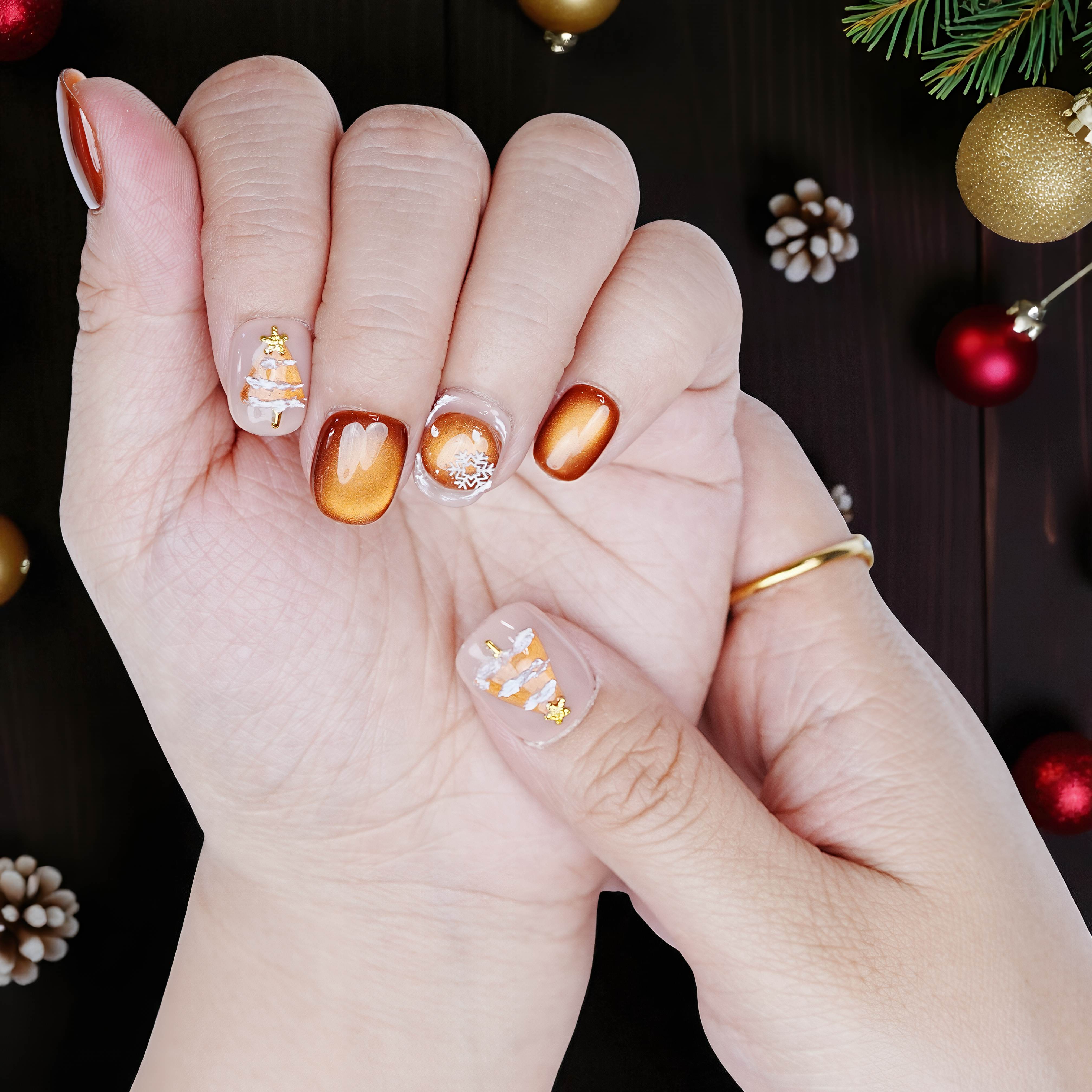 Close-up of hand wearing short bronze shimmer nails with snowflakes and tree accent