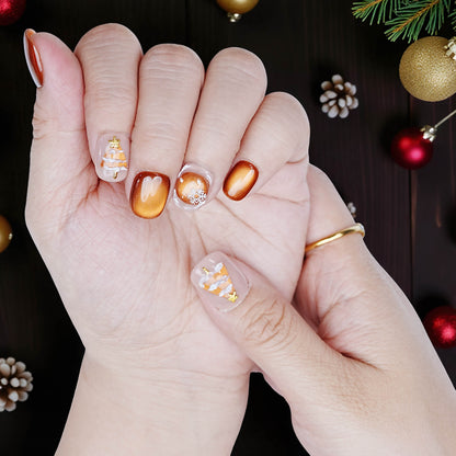 Close-up of hand wearing short bronze shimmer nails with snowflakes and tree accent