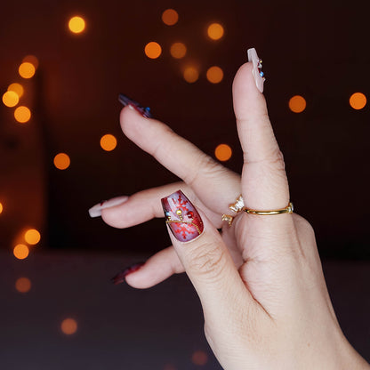 Thumb close-up of red Christmas press on nails with gold chain and tree charm, hand pose with glowing bokeh backdrop