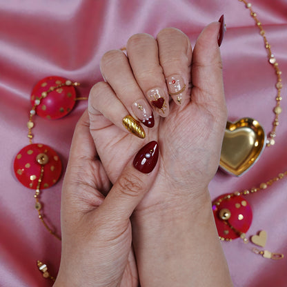 Hand with premium handmade press on nails in red, gold, and nude heart designs on pink satin.