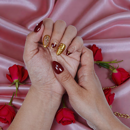 Hand with premium handmade press on nails in red and gold, roses and pink satin background