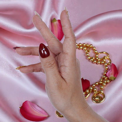 Hand with premium burgundy press on nails and gold jewelry on pink satin with rose petals