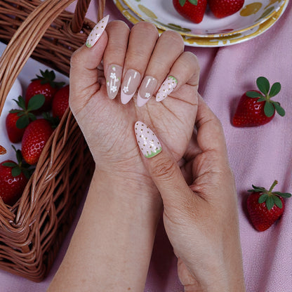 Hand with strawberry-themed handmade press on nails, basket of strawberries in background