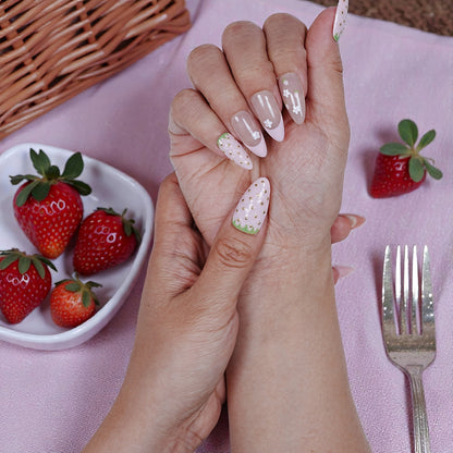 Hand with premium handmade press on nails featuring strawberry designs, beside fresh strawberries.