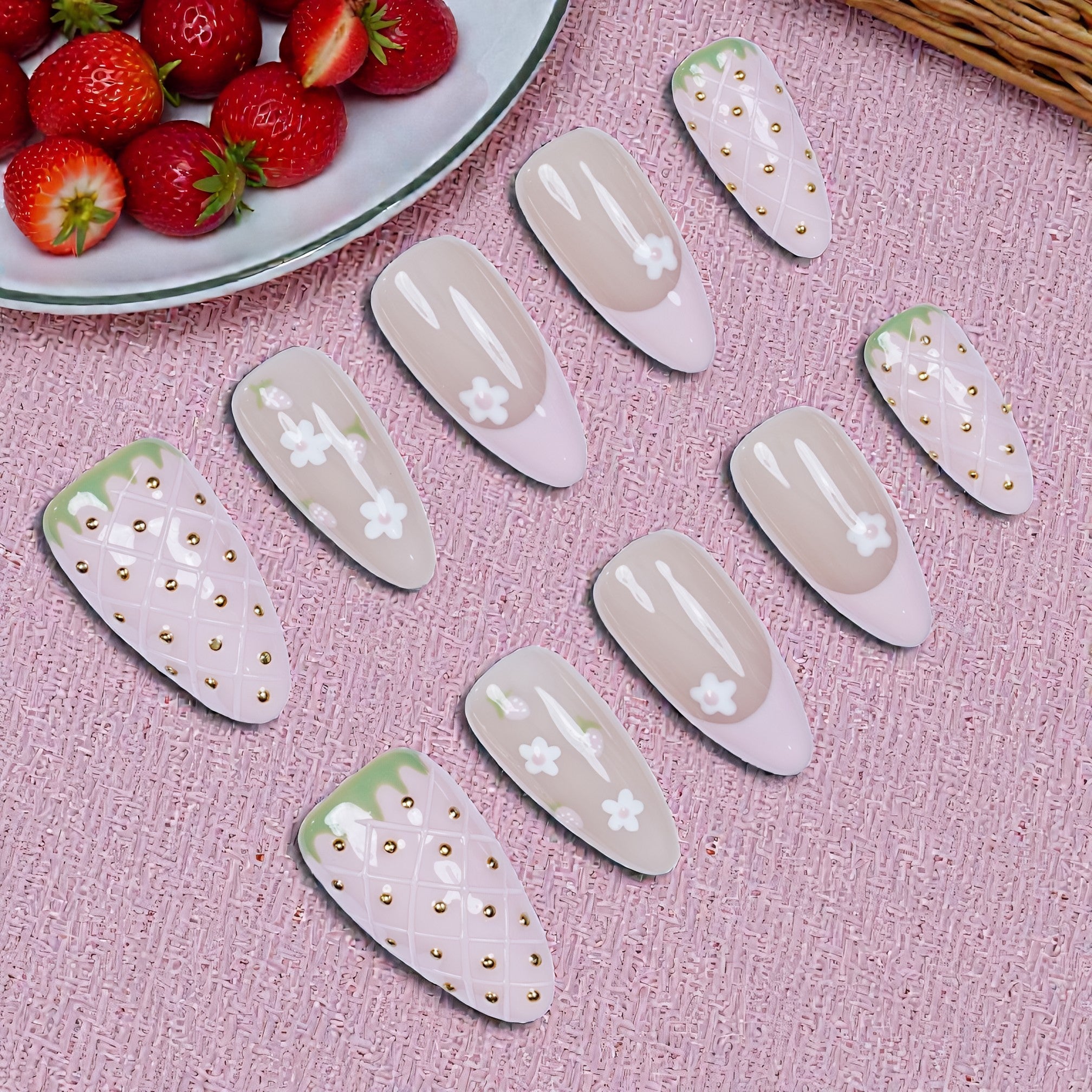 Handmade press on nails with pink floral and strawberry designs on pink textured surface