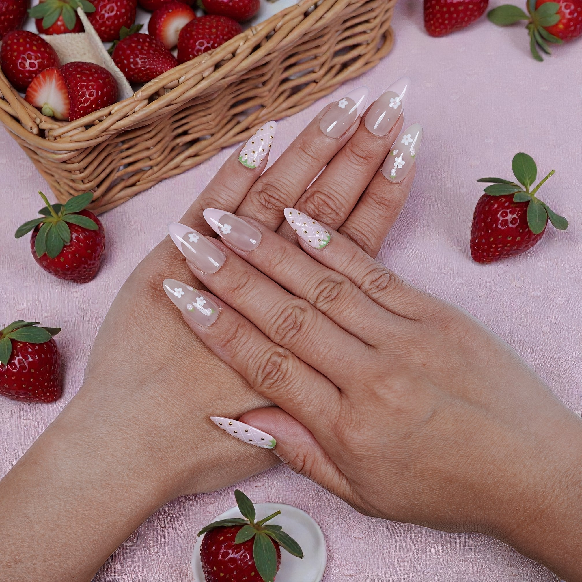 Hands with premium handmade press on nails in strawberry and floral design, strawberries nearby.