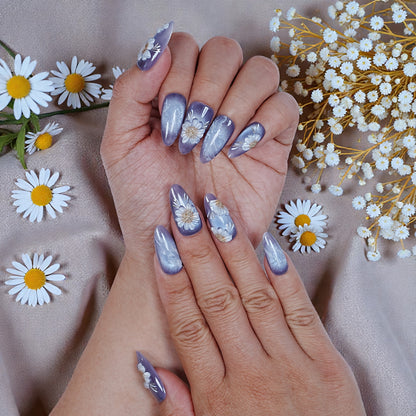 Hand with purple floral press on nails surrounded by daisies on a satin fabric, premium nail art