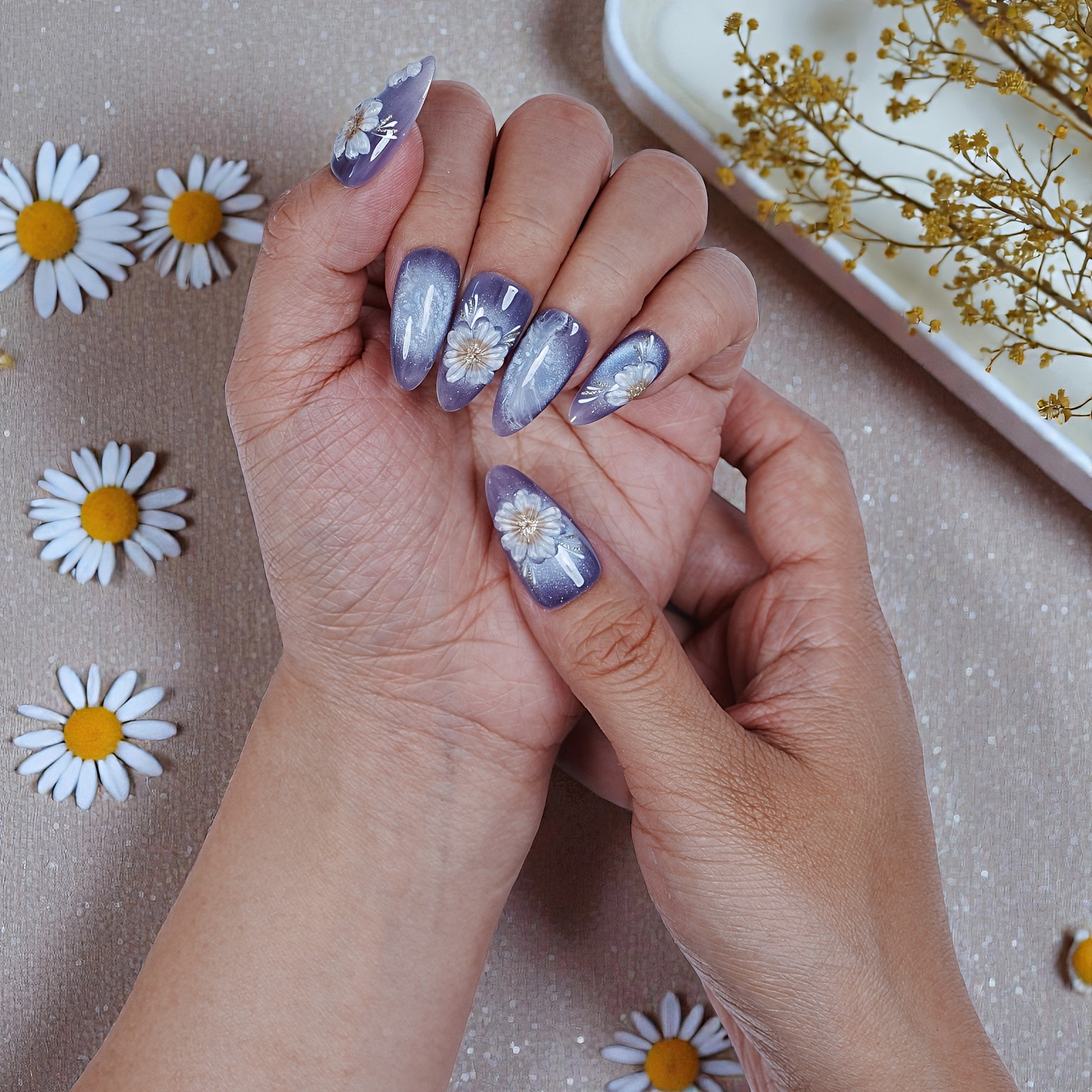 Hand with purple daisy press on nails, floral nail art, on sparkly background with flowers