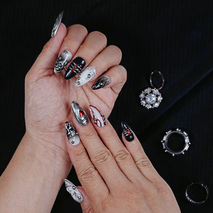 Hand with black, white, and silver 3D press on nails with jewel accents on black background