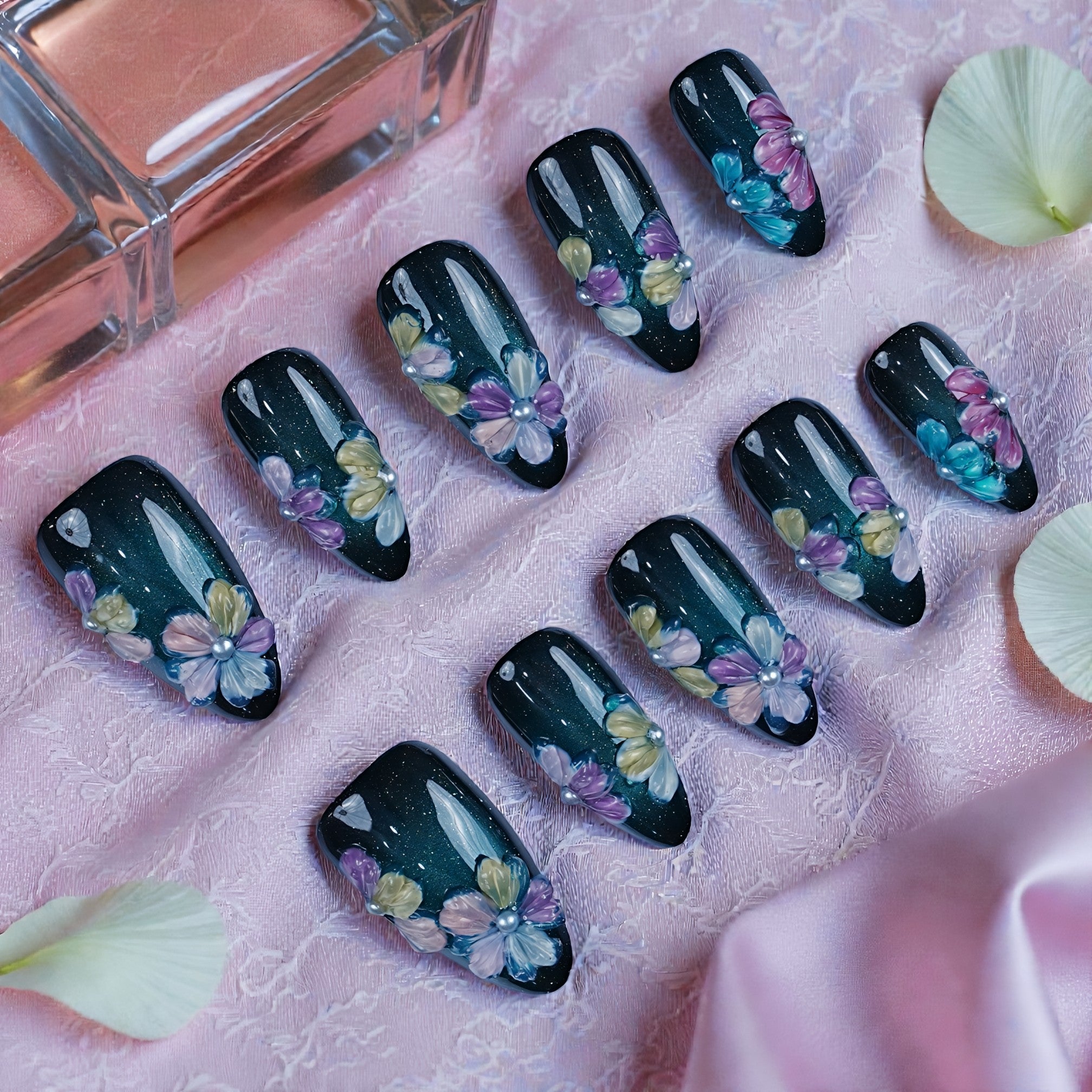 Handmade press on nails with 3D floral designs on a dark base, styled on pink lace fabric.