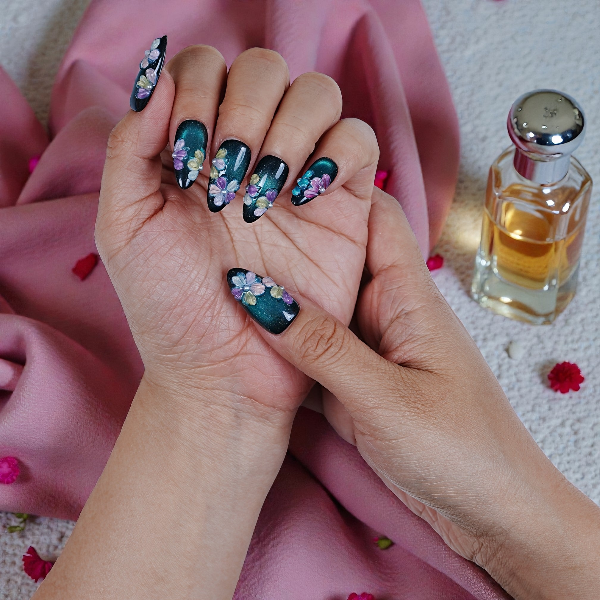 Handmade press on nails with floral 3D art on teal background, styled with perfume bottle