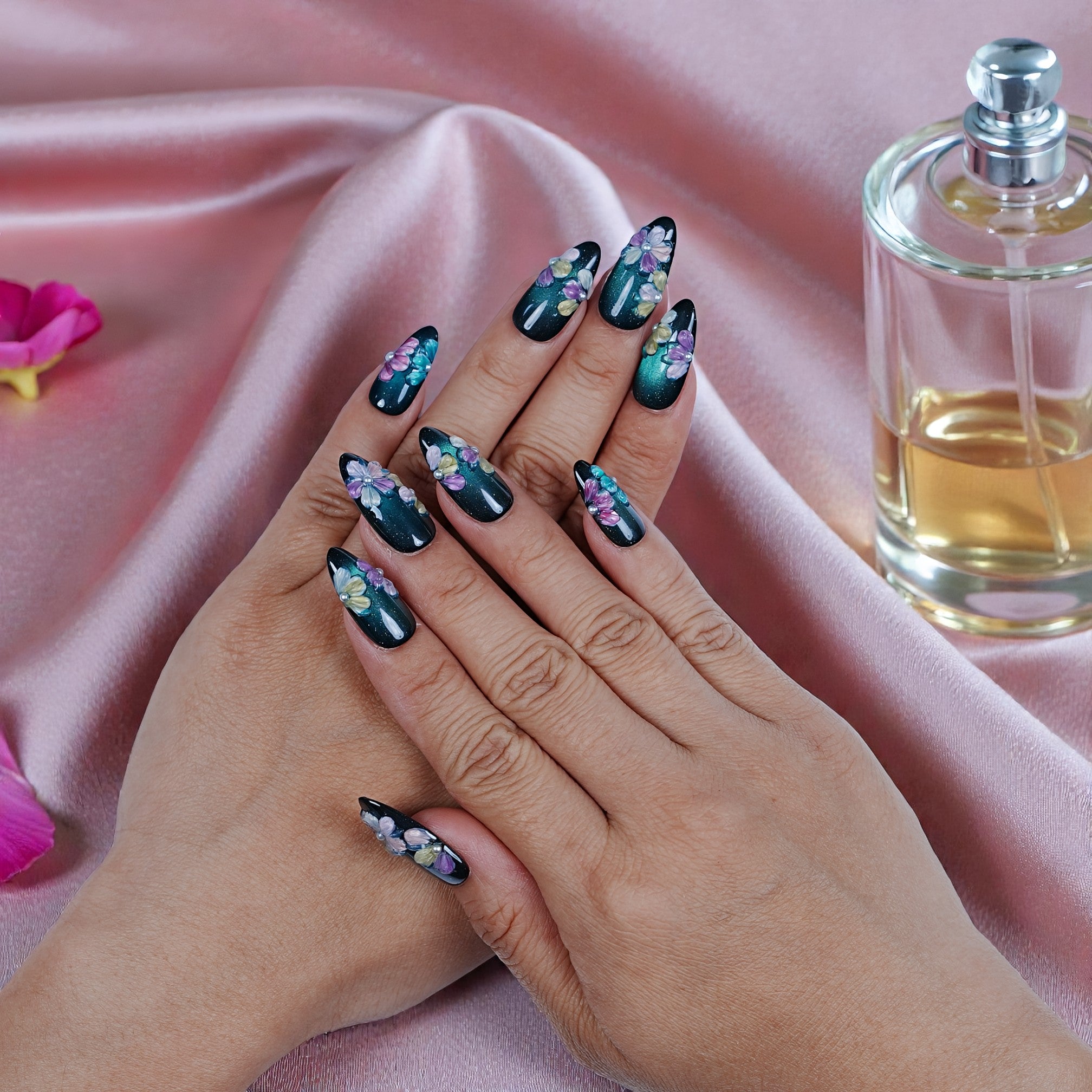 Hand with premium handmade press on nails featuring floral design on a pink satin background