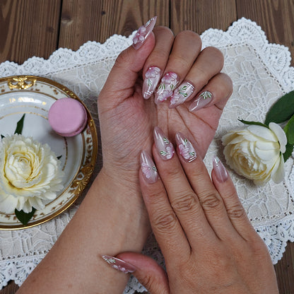 Hand with pink floral handmade press on nails on lace, next to a white rose and dessert