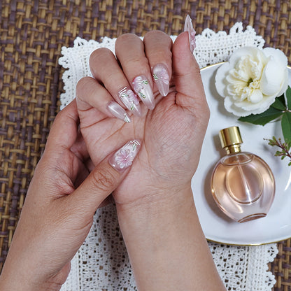Hand with premium handmade press on nails featuring pink floral design, beside perfume bottle and flower