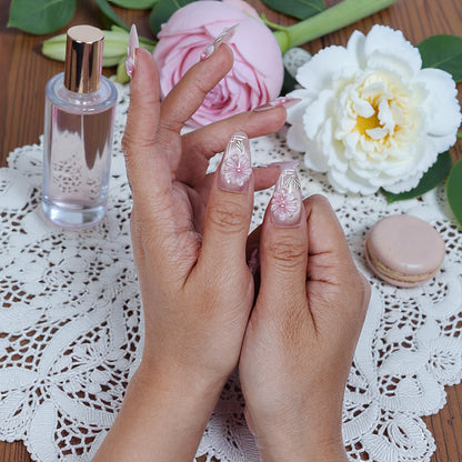 Hand holding premium handmade press on nails with pink floral design, flowers and perfume bottle