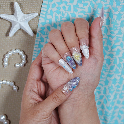 Hand holding premium handmade press on nails with 3D floral and seashell designs, beach theme