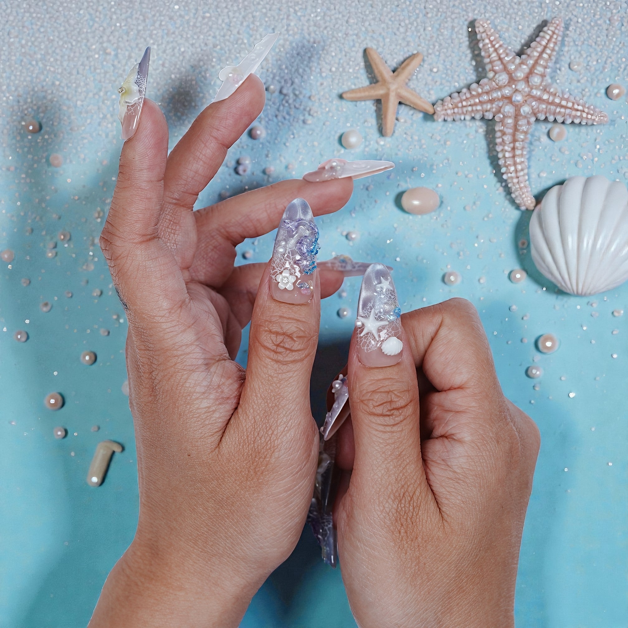 Handmade press on nails with ocean-inspired designs, seashells, and starfish on blue background.
