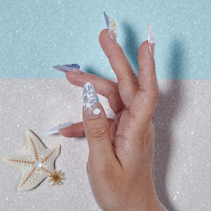 Hand with ocean-themed handmade press on nails and starfish on pastel glitter background