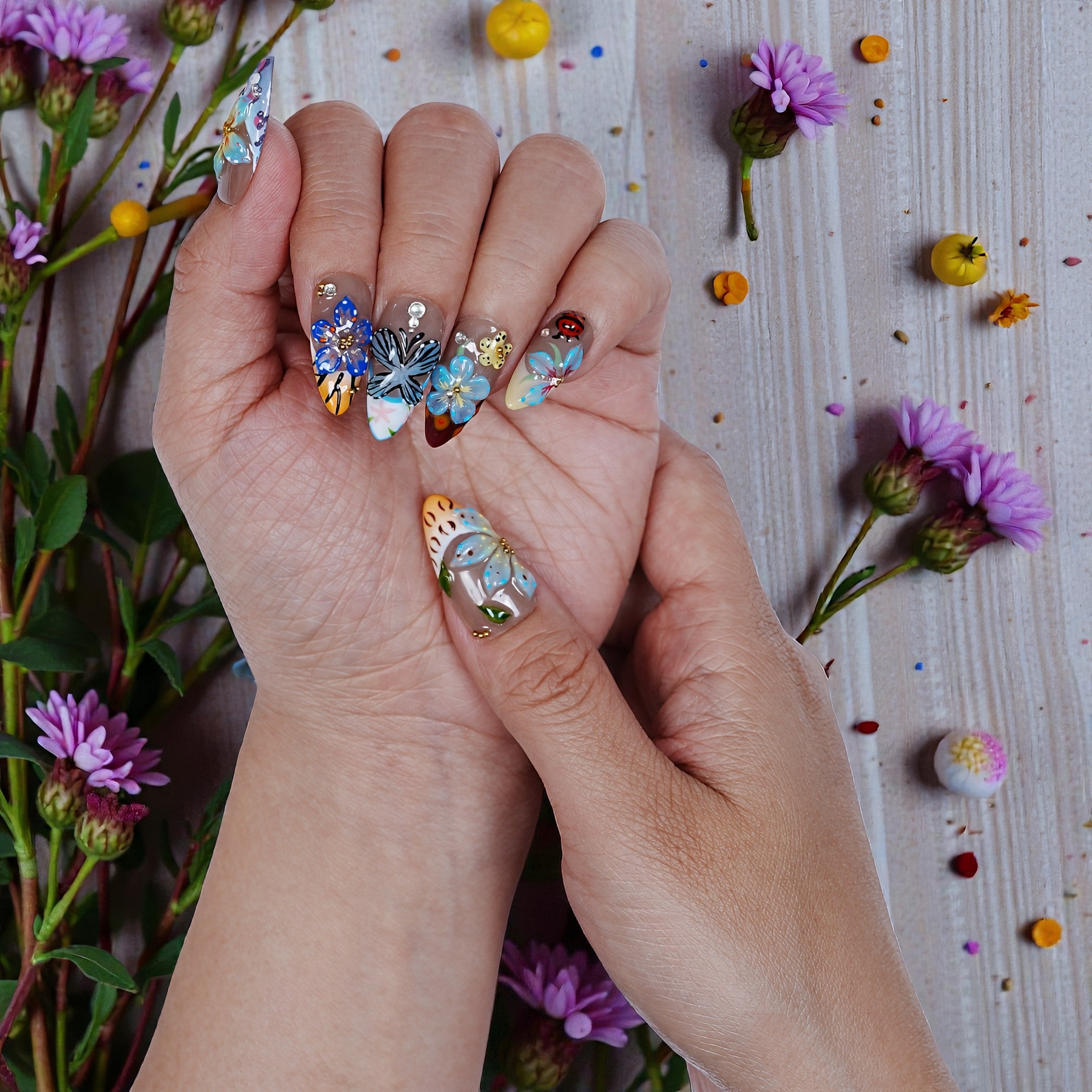 Hand displaying premium handmade press on nails with floral 3D art, surrounded by flowers