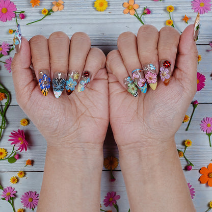 Hands with colorful handmade press on nails featuring 3D floral and butterfly designs