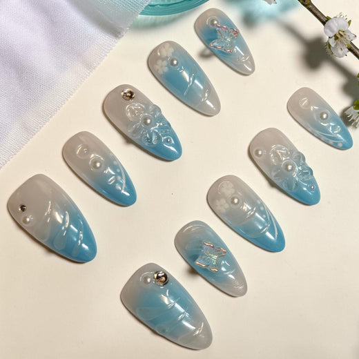 Sky Petal baby blue press on nails, almond set fading from milky white to blue with clear 3D flowers, pearls and iridescent butterflies