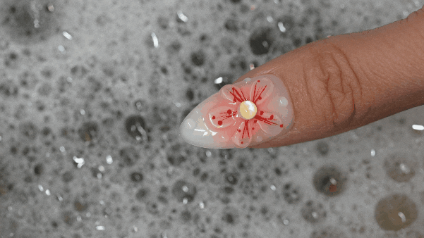 Soaking a floral press on nail in warm soapy water to gently loosen adhesive for easy removal